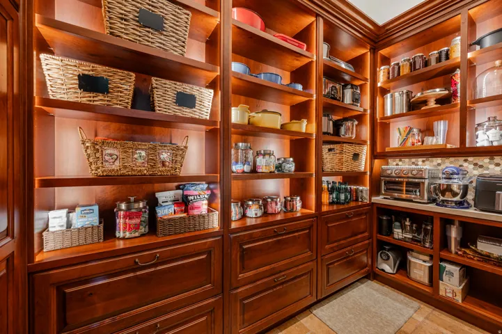 Custom built-in shelving with integrated lighting, rich wood-finish cabinetry, ample storage drawers, countertop space, and a decorative tile backsplash