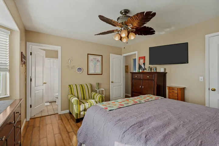 Wood-finish flooring, ceiling fan with integrated lighting, wall-mounted television, and a doorway to a bathroom with tile flooring