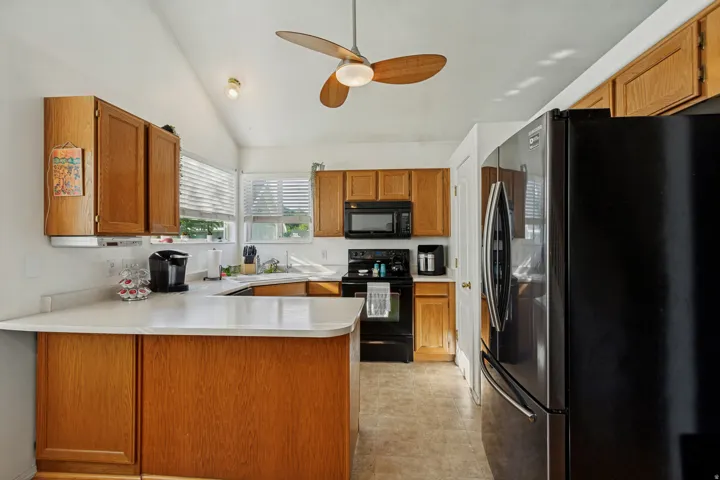 Kitchen featuring wood cabinetry, white countertops, black appliances, and a vaulted ceiling with a ceiling fan