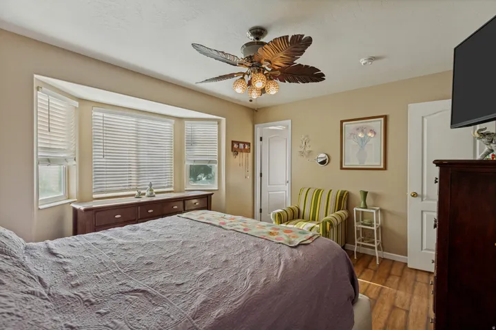 Bay window with blinds, wood-finish flooring, ceiling fan with light fixture, and interior doors