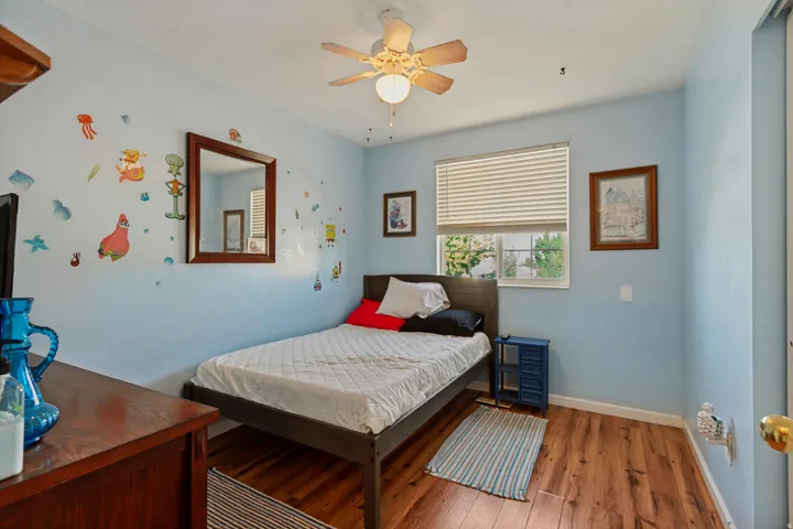 Wood-finish flooring, ceiling fan with integrated lighting, window with blinds, and light blue wall finish