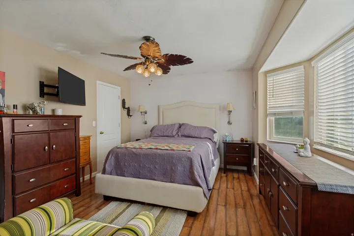 Wood-finish flooring, ceiling fan with integrated lighting, built-in bay window ledge, and wall-mounted sconces