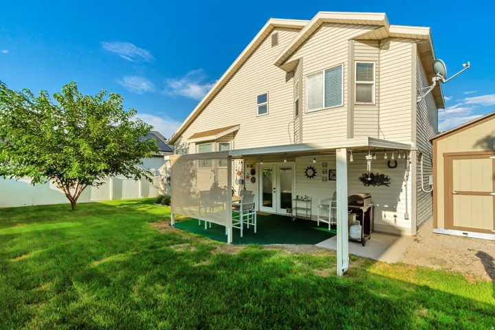 Expansive green lawn with a mature tree, white privacy fencing, covered patio area with a concrete slab, and an exterior storage shed