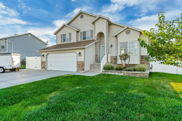 Two-story residence featuring light-toned siding, a two-car garage, stone accents, and a front yard with landscaping