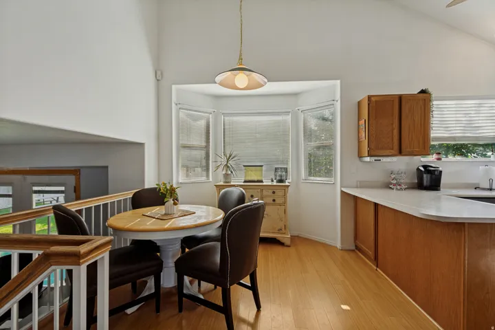 Wood-finish flooring with a bay window, vaulted ceiling, and recessed kitchen cabinetry with light countertops