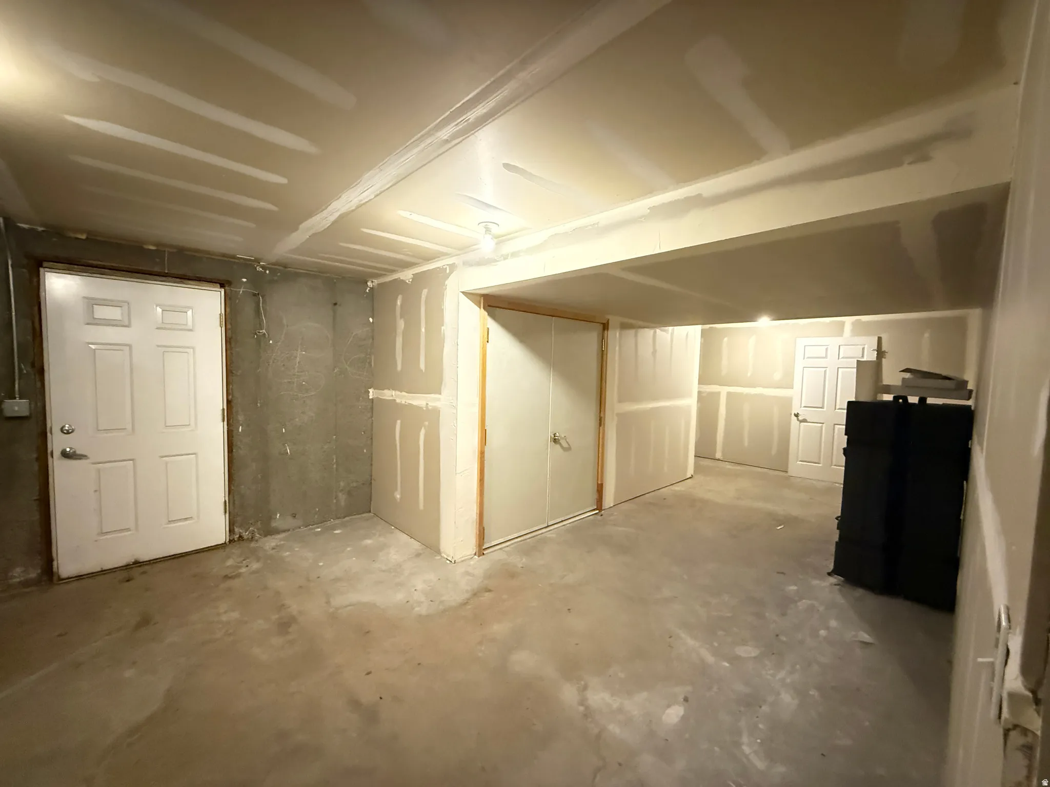 Unfinished basement space with concrete flooring, drywall-finished walls, and multiple internal doors