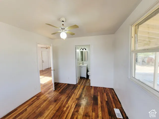 Hardwood flooring, ceiling fan with light fixture, white walls, double-hung window, and bathroom featuring a vanity with vessel sink and wall-mounted light fixture