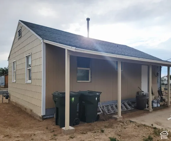Side exterior with a covered patio, neutral-toned siding, and a dark shingle roof