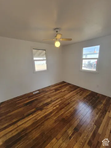 Wood-finish flooring, white walls, two windows, and a ceiling fan with integrated lighting