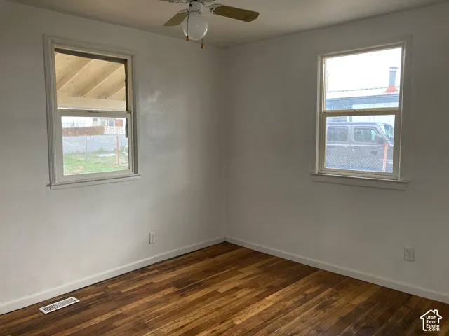 Wood-finish flooring with white baseboards, two windows with white trim, and a ceiling fan with integrated lighting