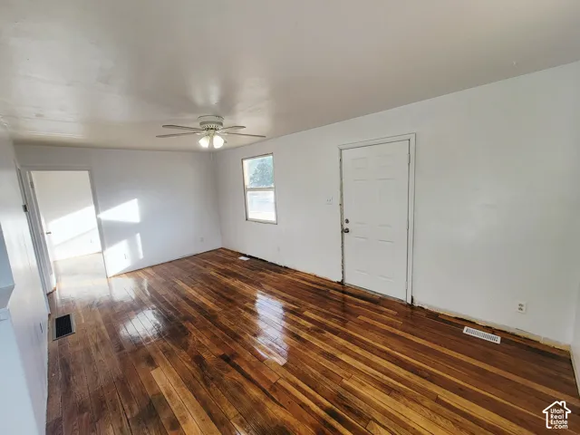 Wood-finish flooring throughout, a white paneled door, a ceiling fan with integrated lighting, and a window