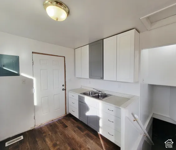 Contemporary kitchen featuring white and gray cabinetry, dual basin stainless steel sink, wood-finish flooring, and light-toned countertops