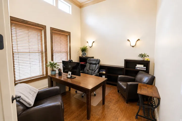 Vaulted ceiling with crown molding, wood-finish flooring, two large windows with wood blinds, custom built-in shelving, and wall sconces