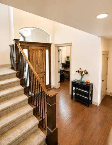 Two-story entryway with wood-finish flooring, a wood front door with sidelights, and a carpeted staircase with an iron spindle railing