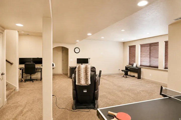 Recessed lighting illuminates a carpeted open-concept space featuring an arched doorway and multiple windows with blinds