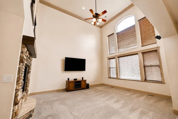 Spacious room featuring vaulted ceilings with exposed wood beams, a ceiling fan with integrated lighting, and abundant natural light from an arched window with wooden blinds