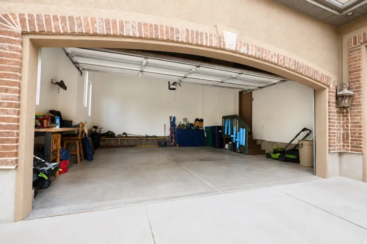Brick archway entrance, concrete flooring, exterior wall sconce, interior wall windows, and overhead garage door mechanism