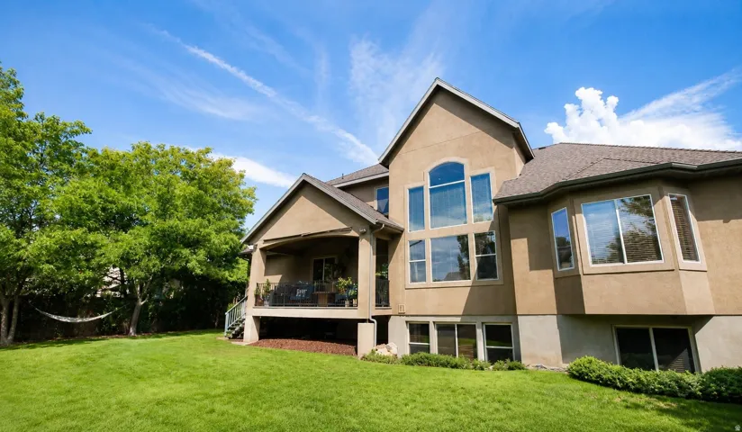 Expansive rear elevation featuring a covered balcony, large picture windows, a bay window, and a sizable lawn area