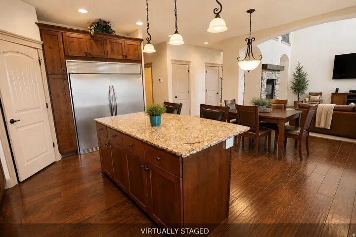 Kitchen island with a light-toned countertop, wood-finish flooring throughout, stainless steel refrigerator, and wood-finish cabinetry