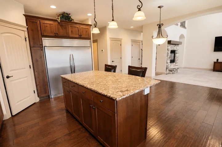 Kitchen island featuring a granite countertop, wood-finish flooring, and built-in stainless steel refrigerator