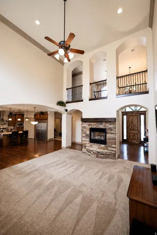 Vaulted ceiling with a ceiling fan, stone-faced fireplace, wrought iron railings, and wood-finish flooring
