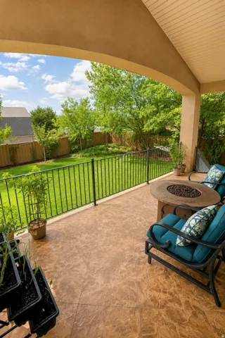 Covered patio with a textured concrete floor, black metal railing, and an expansive lawn beyond