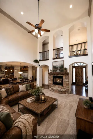 Two-story living area featuring a stone-clad fireplace, high vaulted ceilings, and a decorative wood-bladed ceiling fan