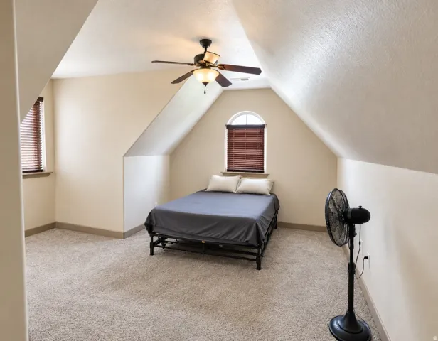 Carpeted room with sloped ceilings, arched window with horizontal blinds, and a ceiling fan with integrated lighting