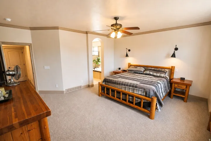 Carpeted flooring, ceiling fan with integrated lighting, wall-mounted sconce lighting, and an arched entry
