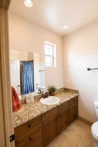 Warm wood-finish cabinetry with a granite countertop, undermount sink, and recessed lighting