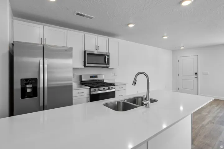 Kitchen featuring a stainless steel appliance suite, white cabinetry, recessed lighting, and a double basin stainless steel sink