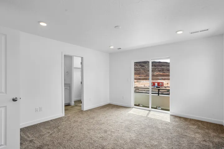 Plush carpet flooring, recessed lighting, white trim, and a sliding glass door opening to a balcony with a black metal railing