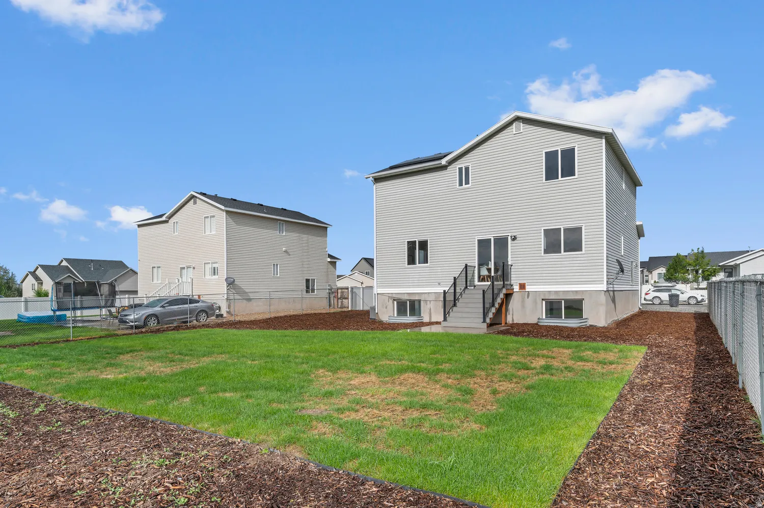 Expansive backyard featuring a manicured lawn, wood chip landscaping, and chain-link fencing