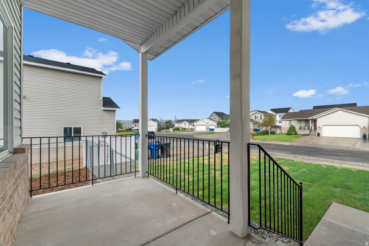 Covered concrete porch featuring black metal railings and a brick facade accent