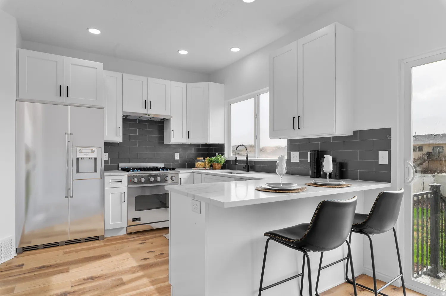 Kitchen featuring white cabinetry, stainless steel appliances, dark subway tile backsplash, light-toned wood-finish flooring, and a kitchen island with seating