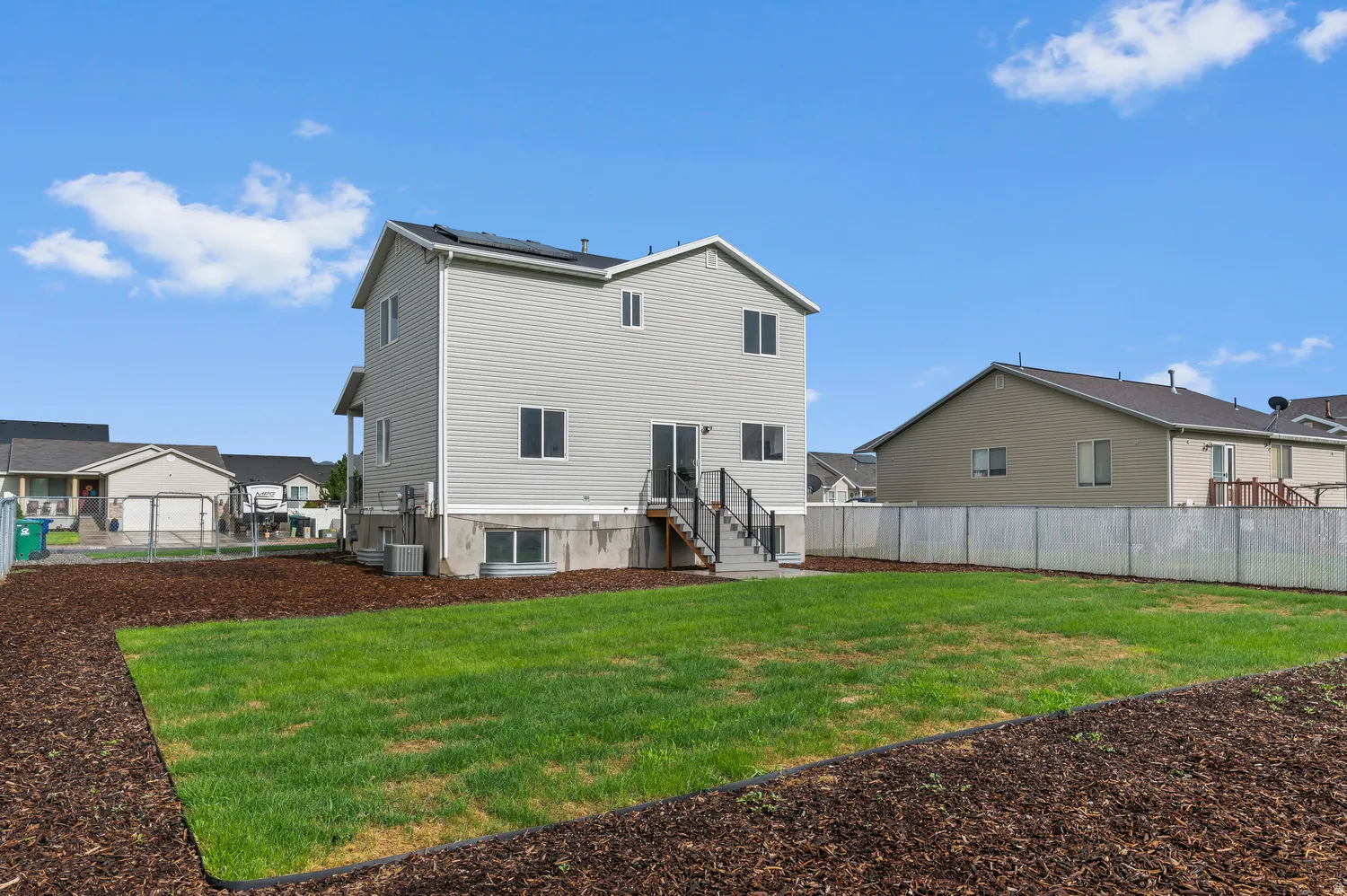Expansive backyard featuring a manicured lawn, wood chip landscaping, and a privacy fence