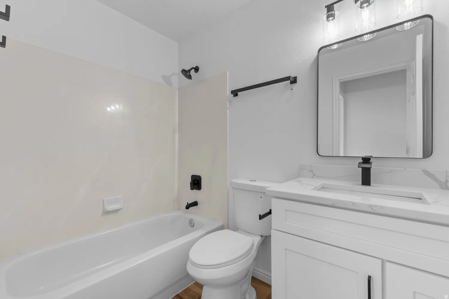 Bathroom featuring a white vanity with a rectangular sink, a framed mirror, a modern three-light fixture, a toilet, and a combination tub and shower with matte black fixtures