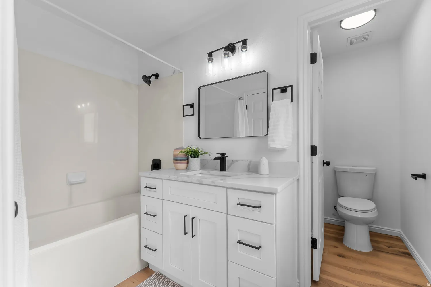White vanity with integrated sink, black fixtures, and a rectangular mirror
