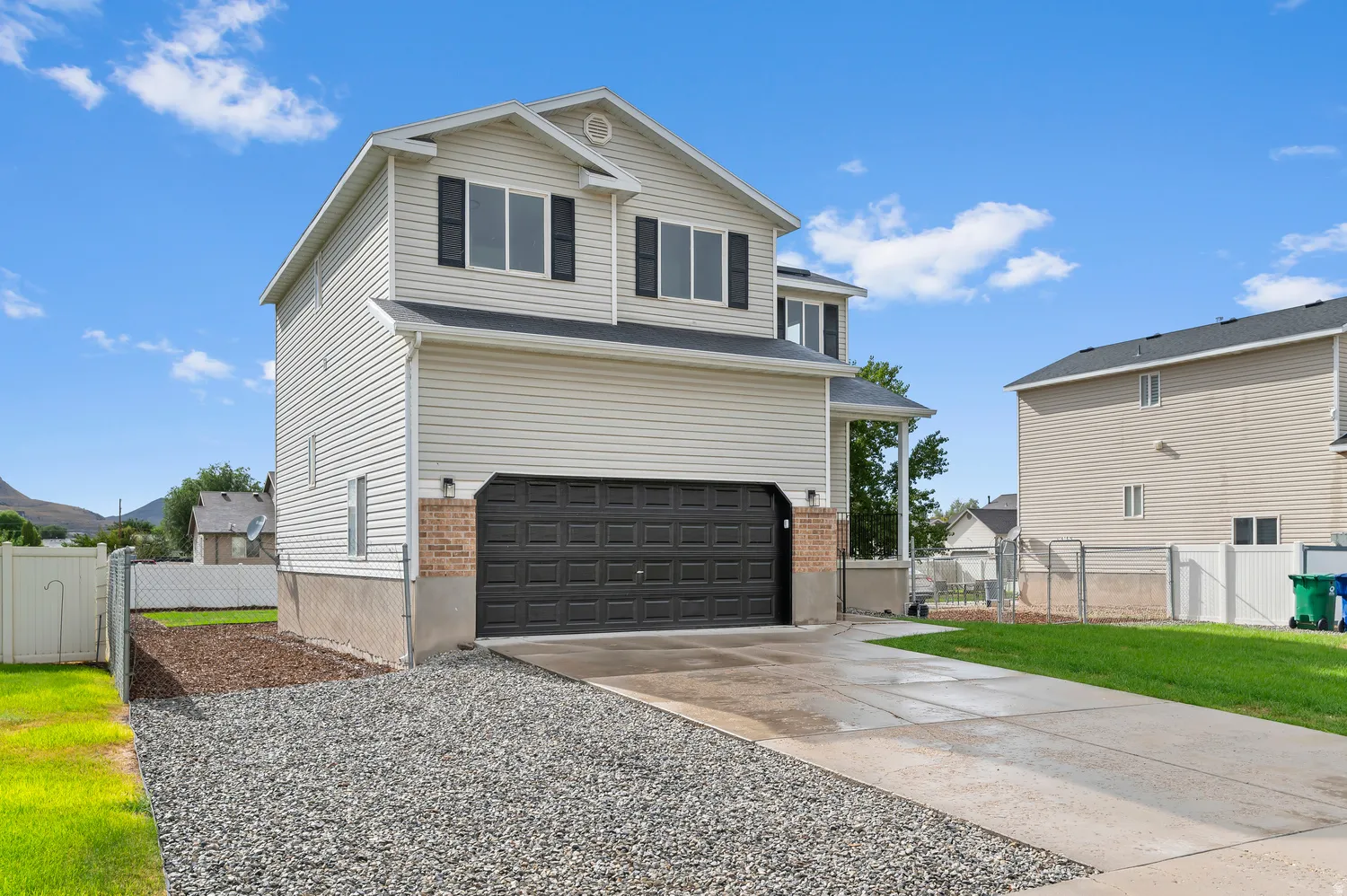 Two-story residence featuring light-colored siding, a dark garage door, and a concrete driveway