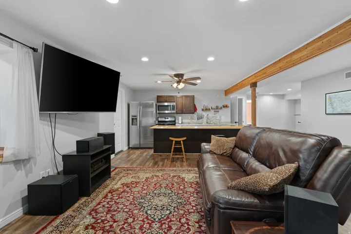 Open-concept living area with wood-finish flooring, a wood beam ceiling accent, recessed lighting, and a ceiling fan