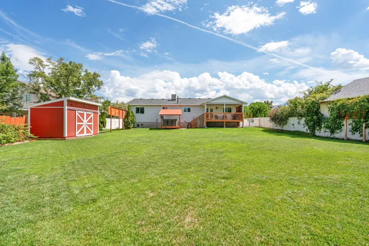 Expansive grassy yard featuring a red storage shed, a wood deck with a covered portion, and perimeter fencing