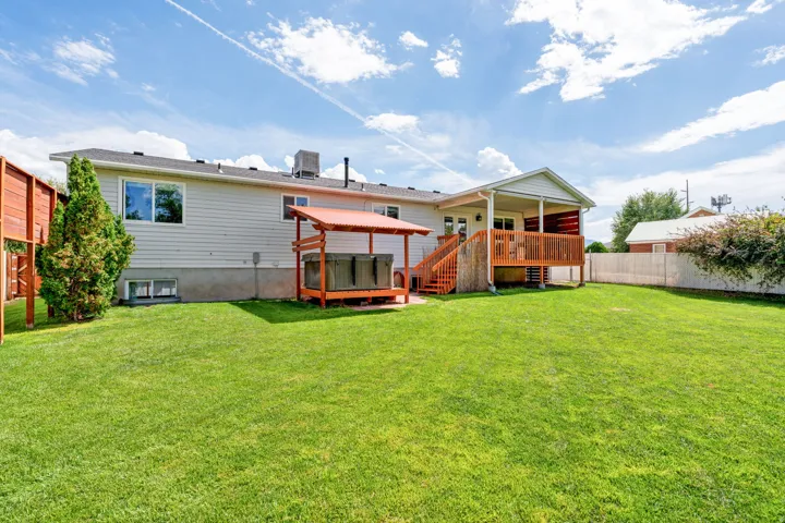 Expansive backyard with a green lawn, wood-decked patio, and a covered hot tub area