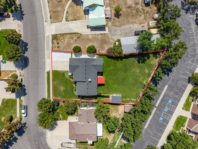 Expansive property featuring a dark-shingled roof, a paved driveway, a verdant lawn, and mature perimeter trees