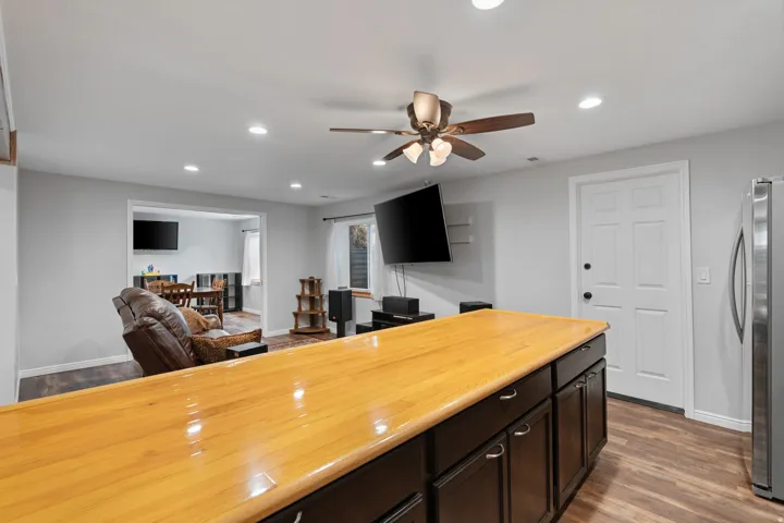 Kitchen island with a polished wood-finish countertop and dark cabinetry, stainless steel refrigerator, and wood-finish flooring