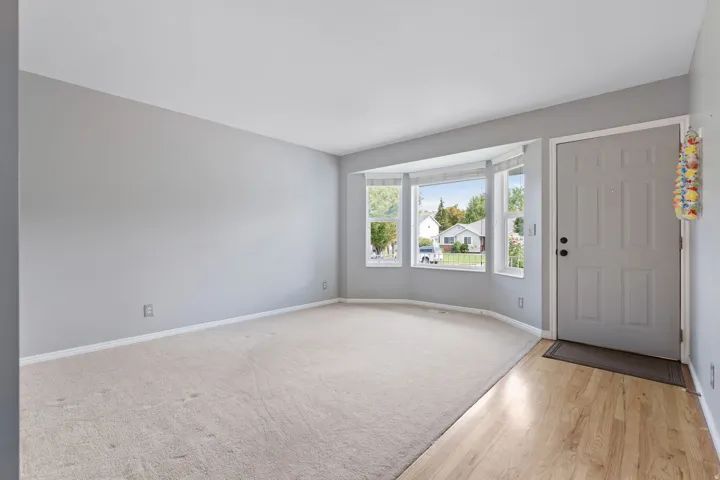 Bay window with multiple panes, light gray wall paint, light-toned carpet, and wood-finish flooring