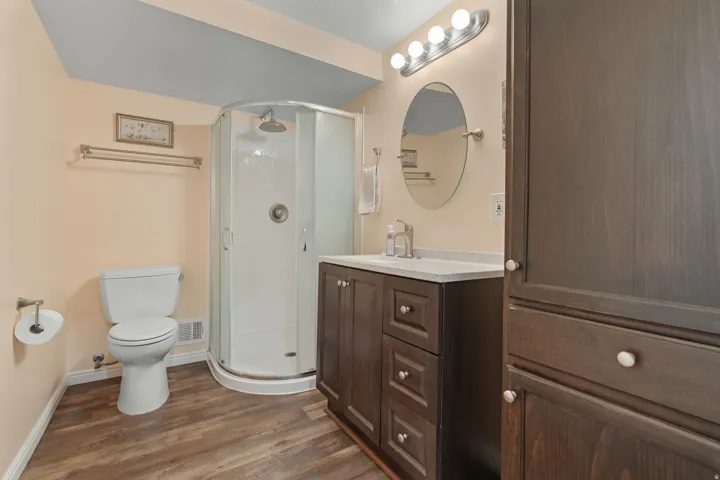 Wood-finish flooring, dark wood-finish vanity with countertop, round glass shower enclosure, and built-in dark wood-finish cabinetry