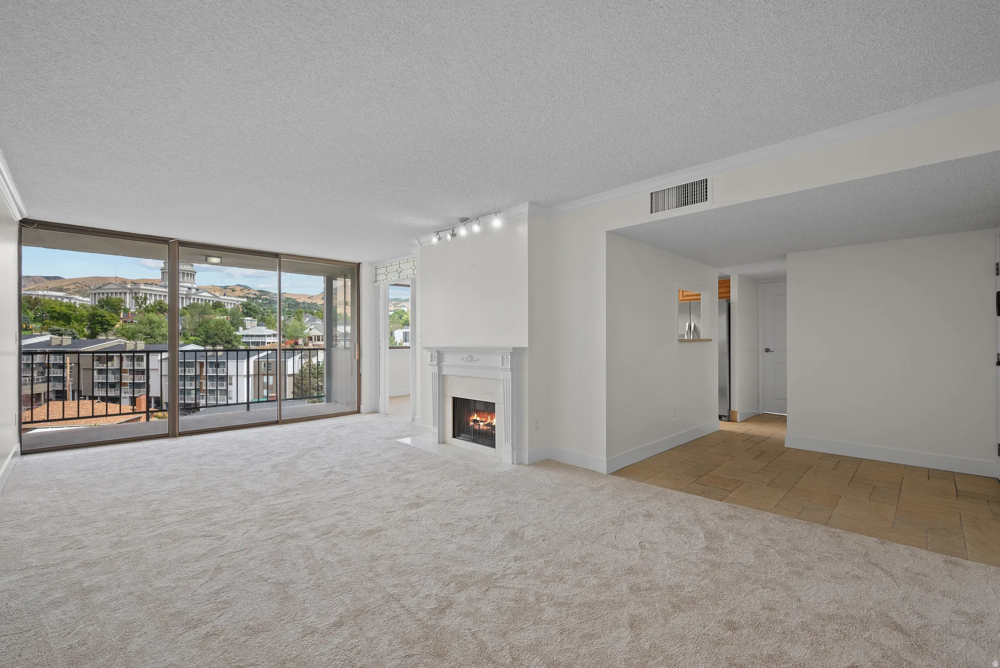 Expansive living area with neutral carpeting, a decorative fireplace, and track lighting