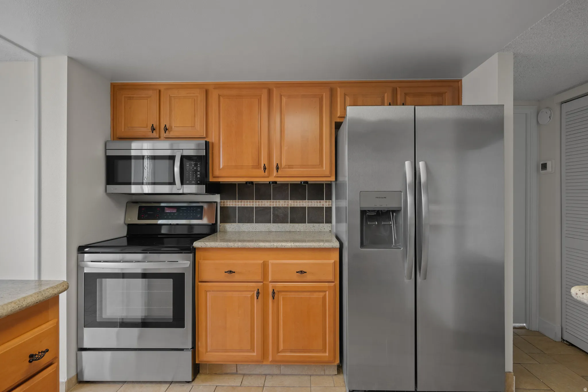 Stainless steel appliances, wood cabinetry, tile backsplash, and light-toned countertops