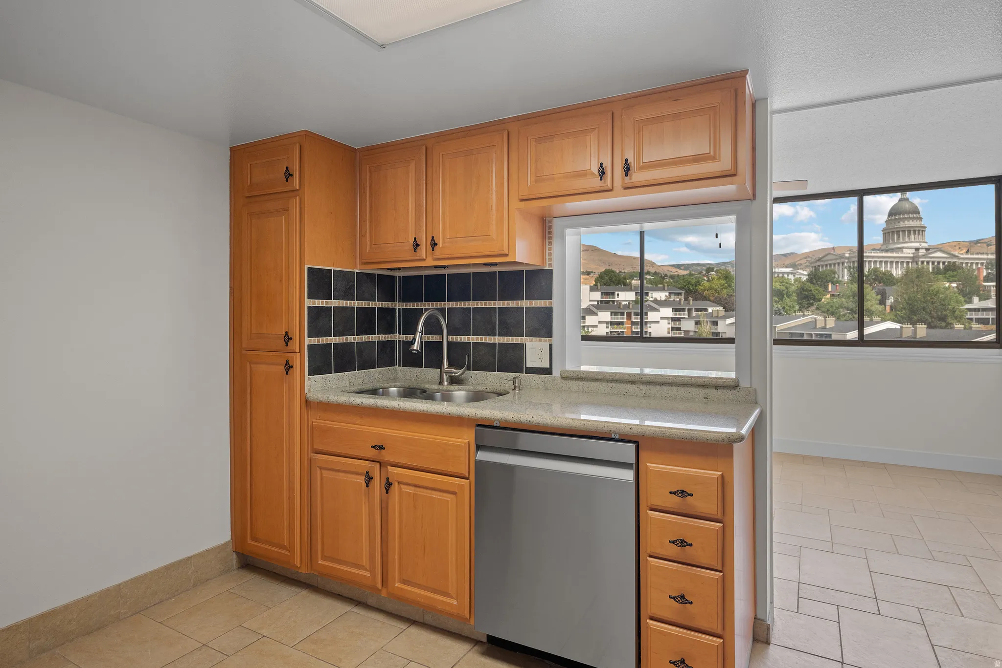 Kitchen featuring wood cabinetry, stainless steel dishwasher, double basin sink, and a black tile backsplash