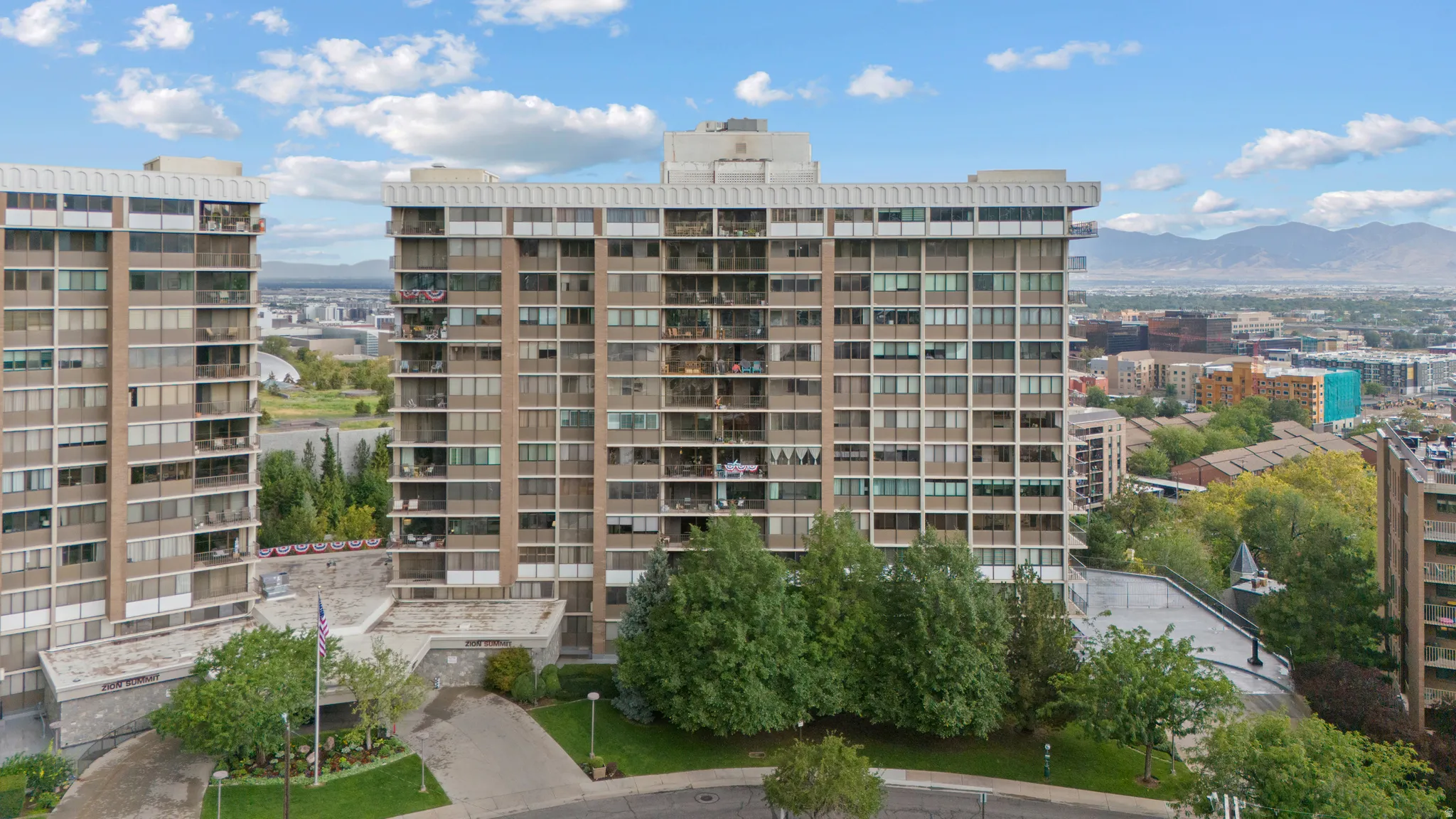 High-rise residential building featuring multiple balconies, a structured facade, and surrounding green landscaping